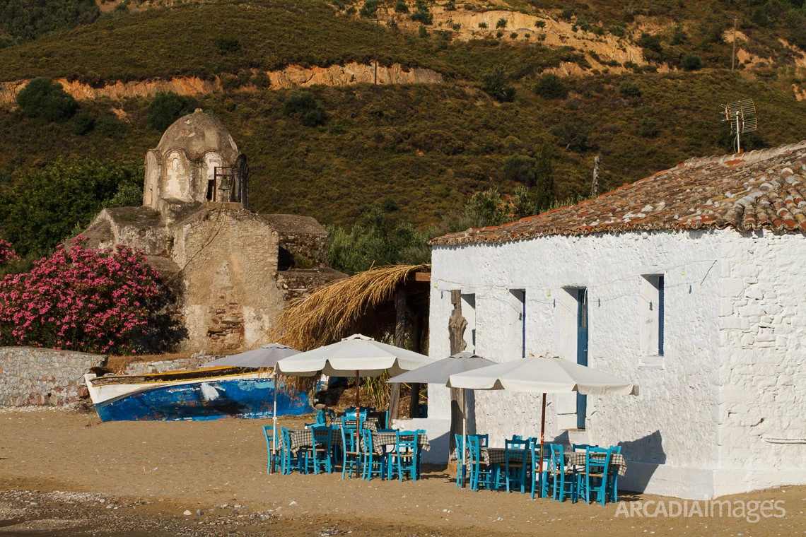 The chairs of a fish tavern and the Byzantine church of Aghia Varvara in the background. Skoutari, Laconia, Peloponnese