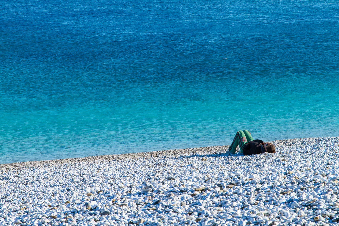 A woman enjoys the sun at Halikia-Vata pebble beach. Kotronas, Mani, Peloponnese, Greece